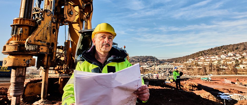 Bild unseres Kollegen auf der Baustelle vor einem Bagger.
